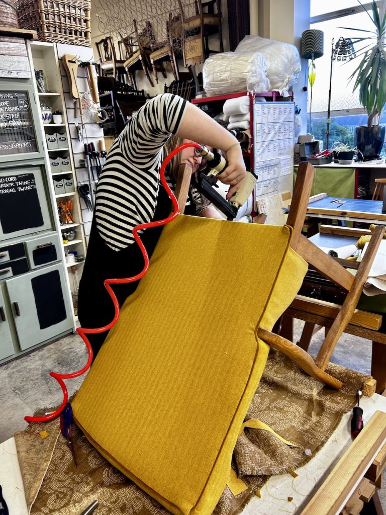 Student adding finishing touches to a chair using a pneumatic stapler inside the Stevenson & Soames upholstery workshop.