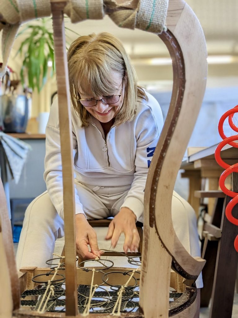 Student learning to traditionally lash upholstery springs inside a chair frame as part of a hands on course.